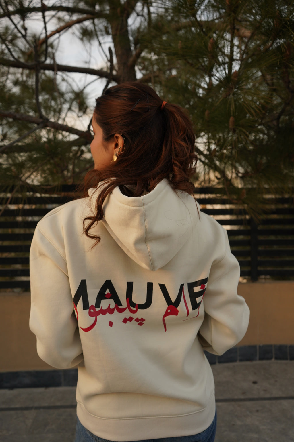 A person wearing a white hoodie with the brand name 'MAUVE' written on the back in bold letters.