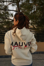 A person wearing a white hoodie with the brand name 'MAUVE' written on the back in bold letters.